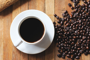 A cup of black coffee with roasted beans on wood table