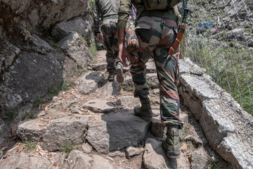 Indian soldiers are walking along a mountain trail up. Back view.