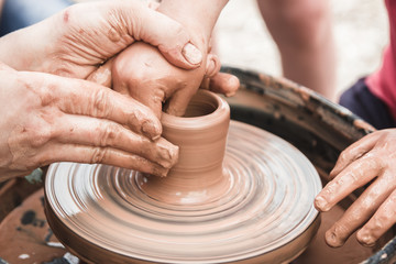 A close up view on ceramic production process on potter's wheel with children. Clay crafts with kids concept.