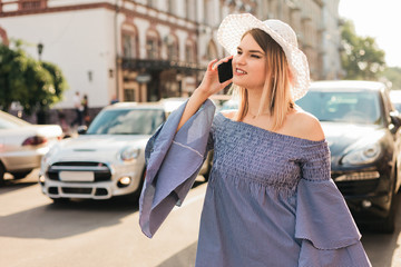 Young attractive woman calls taxi on the phone on the roadway in the city. Hitchhiking concept