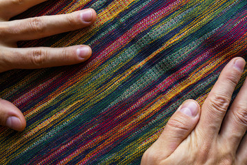 Man hands on motley striped fabric cloth material closeup. Tapestry background top view