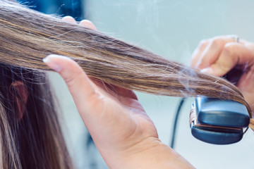 Hairdresser using flat iron on hair of woman customer
