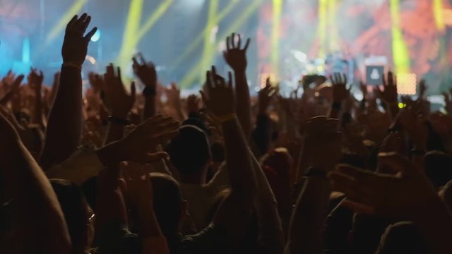 Happy people watching an amazing musical concert. Fans raise their hands up and making photos with mobile phone. 4k, UHD