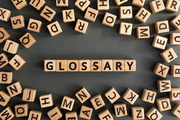 Glossary - word from wooden blocks with letters, alphabetical list with words meanings dictionary glossary  concept, random letters around, top view on grey background - obrazy, fototapety, plakaty