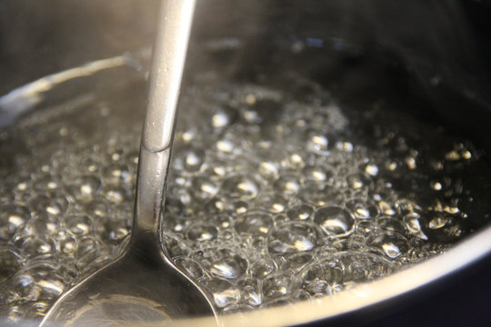 ladle in bubbles of clear boiling sugar syrup in stainless steel pot