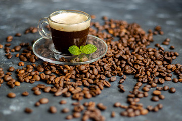 A cup of delicious, aromatic coffee. It is on a substrate of coffee beans. Has a lush, white foam. Decorated with mint leaves. 
