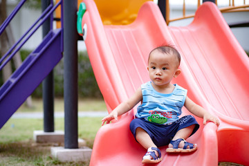 Fototapeta na wymiar Nonthaburi, Thailand, Aug 28, 2019 - Little baby boy sitting on slider in public park