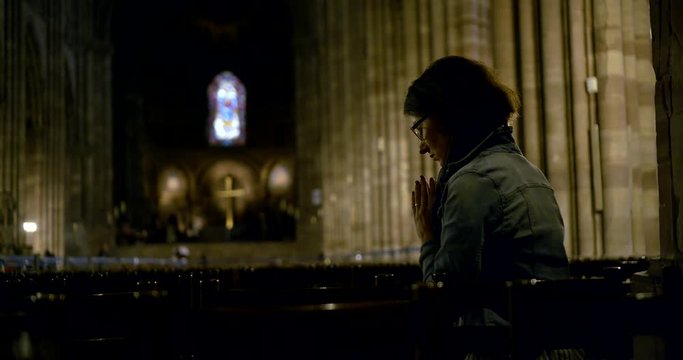 middle aged female prayer is sitting alone in catholic church, saying grace for God