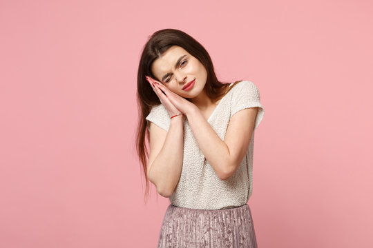 Young woman in casual light clothes posing isolated on pastel pink wall background, studio portrait. People sincere emotions lifestyle concept. Mock up copy space. Sleep with folded hands under cheek.