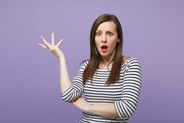 Shocked irritated young woman in casual striped clothes posing isolated on violet purple background studio portrait. People lifestyle concept. Mock up copy space. Keeping mouth open, spreading hands.