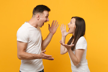 Excited young couple two friends guy girl in white empty blank t-shirts posing isolated on yellow orange background. People lifestyle concept. Mock up copy space. Looking at each other speading hands.