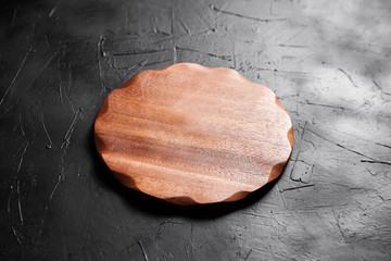 Cutting board on black stone table. Empty round wooden chopping board on dark background