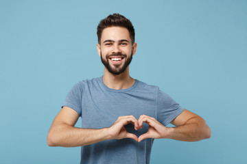 Young smiling handsome man in casual clothes posing isolated on blue wall background, studio portrait. People lifestyle concept. Mock up copy space. Showing shape heart with hands, heart-shape sign.