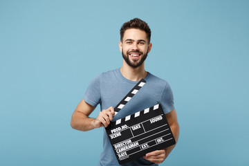 Young smiling man in casual clothes posing isolated on blue wall background, studio portrait. People lifestyle concept. Mock up copy space. Holding in hands classic black film making clapperboard.