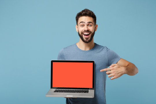 Young excited man in casual clothes posing isolated on blue wall background in studio. People lifestyle concept. Mock up copy space. Point index finger on laptop pc computer with blank empty screen.