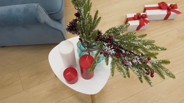 Christmas spruce twig in vase decorated with beautiful toys standing on the table between red candles