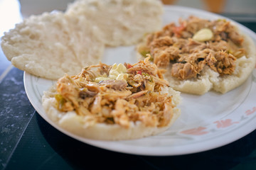 Arepas with shredded chicken, butter and cheese. Hot, you can see the steam and the butter melting. Served on a white plate.