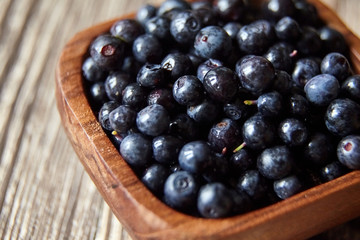 Bilberries closeup in a bowl on brown wooden background. Fresh dark berries on table