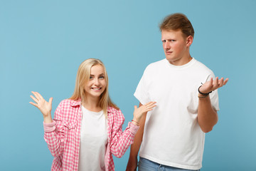 Young fun couple two friends guy girl in white pink empty blank design t-shirts posing isolated on pastel blue background studio portrait. People lifestyle concept. Mock up copy space. Looking camera.