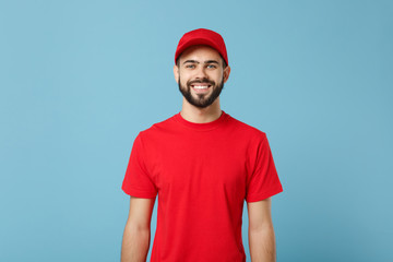Delivery man in red uniform workwear isolated on blue wall background, studio portrait. Professional male employee in cap t-shirt print working as courier dealer. Service concept. Mock up copy space. - obrazy, fototapety, plakaty