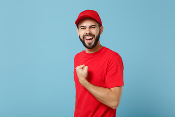 Delivery man in red uniform workwear isolated on blue wall background, studio portrait. Professional male employee in cap t-shirt print working as courier dealer. Service concept. Mock up copy space.