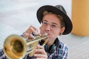 White boy with glasses and a black hat blowing a trumpet with the background out of focus. Concept...