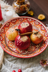 baked apples with cottage cheese and cocoa on a beautiful red plate with a pattern on a brown wooden background and beige gauze fabric