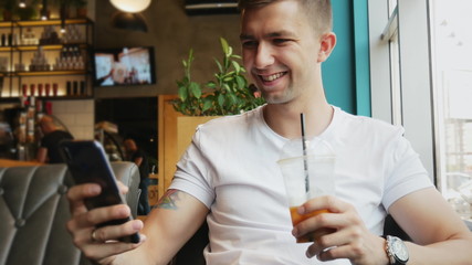 Young businessman uses mobile phone in cafe, drinks cold coffee cocktail, smiles