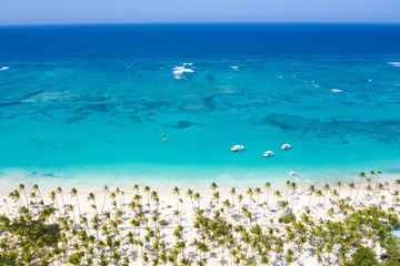 Aerial view from drone on tropical coastline with coconut palm trees, sunbeds and boats floating in caribbean sea - obrazy, fototapety, plakaty