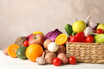 Wicker basket, vegetables and fruits on white wooden background, space for text