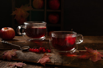 Two red cups with hot fruit drink, apples, autumn leaves, red berries. Still life in vintage stile