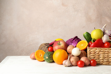 Wicker basket, vegetables and fruits on white wooden background, space for text