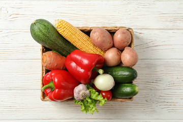 Wicker basket with vegetables on white wooden background, copy space