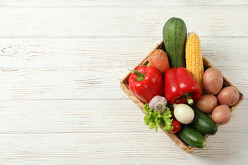 Wicker basket with vegetables on white wooden background, copy space