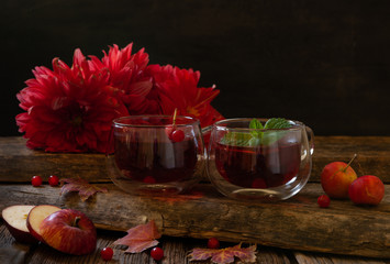 Two red cups with hot fruit drink, apples, autumn leaves, red berries and red dahlias. Still life in vintage stile