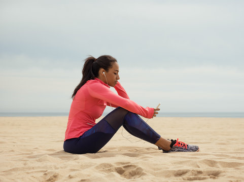 Black sportswoman using phone on beach