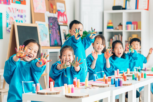 Preschool kids in smock showing finger paint on hands in classroom