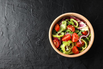 Wooden plate with salad on black background, top view