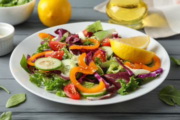 Plate with salad and ingredients on wooden background, close up