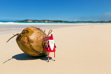 Greeting card with Santa toy and coconut on beach close to sea