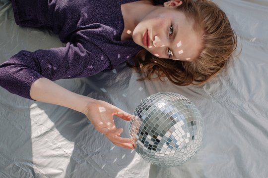 Girl laying on the floor with disco ball among little light reflections