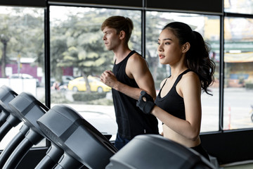 Fototapeta na wymiar Young woman and man running side by side on modern electric treadmills.