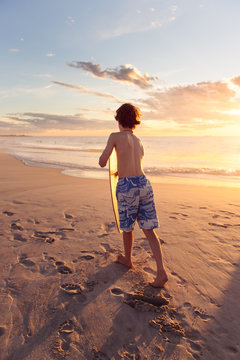 Boy with a skim board at the beach at sunset