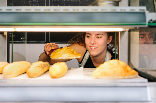 Young woman taking a Cornish Pastie from an oven in a small bakery