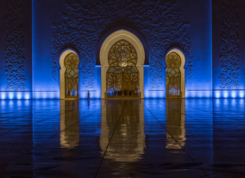 A man in traditional dress walks by the entrance of the Sheikh Zayed Grand Mosque, Abu Dhabi, UAE at night