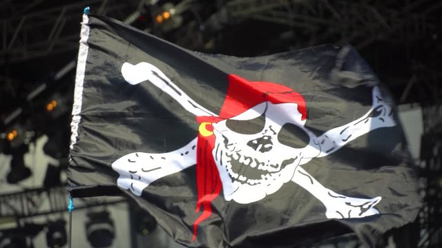black and white pirate flag with skull and crossbones, developing in wind.