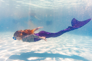 Girl on family vacation swimming gracefully in pool wearing mermaid costume