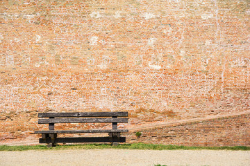 Old wooden bench in front of a brick wall.