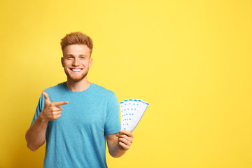 Portrait of happy young man with lottery tickets on yellow background - obrazy, fototapety, plakaty