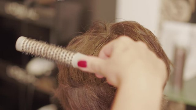 Hairdresser blow-drying hair by styler-dryer, paddle brush on woman head, adding volume to hair for styling haircut in hairdressing beauty saloon. Barber hands blowing wave after haircut in barbershop